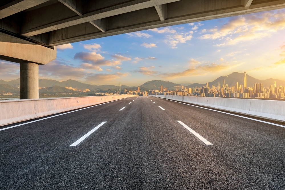 Skyline de Shenzhen : Autoroute moderne et coucher de soleil doré. Autoroute moderne sous un pont en direction du skyline de Shenzhen et ses gratte-ciel, baignée par la lumière du soleil couchant.