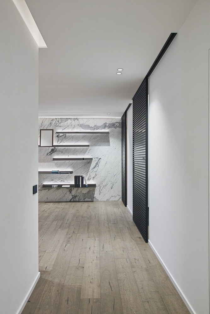Couloir minimaliste de luxe : marbre veiné et porte coulissante noire. Design intérieur minimaliste. Couloir élégant avec mur d'accent en marbre veiné, étagères lumineuses et porte coulissante noire à lames.