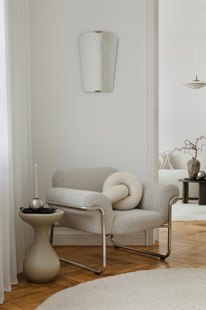 Fauteuil bouclette design : déco moderne et élégante Fauteuil design en bouclette beige et chrome avec coussin noué. Miroir à motif, table d'appoint taupe. Ambiance neutre.