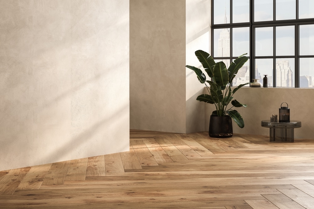 Parquet bois clair et mur texturé : ambiance loft urbain Mur texturé beige et parquet bois chevrons baignés de lumière. Grande baie vitrée urbaine. Plante tropicale et table en verre fumé.