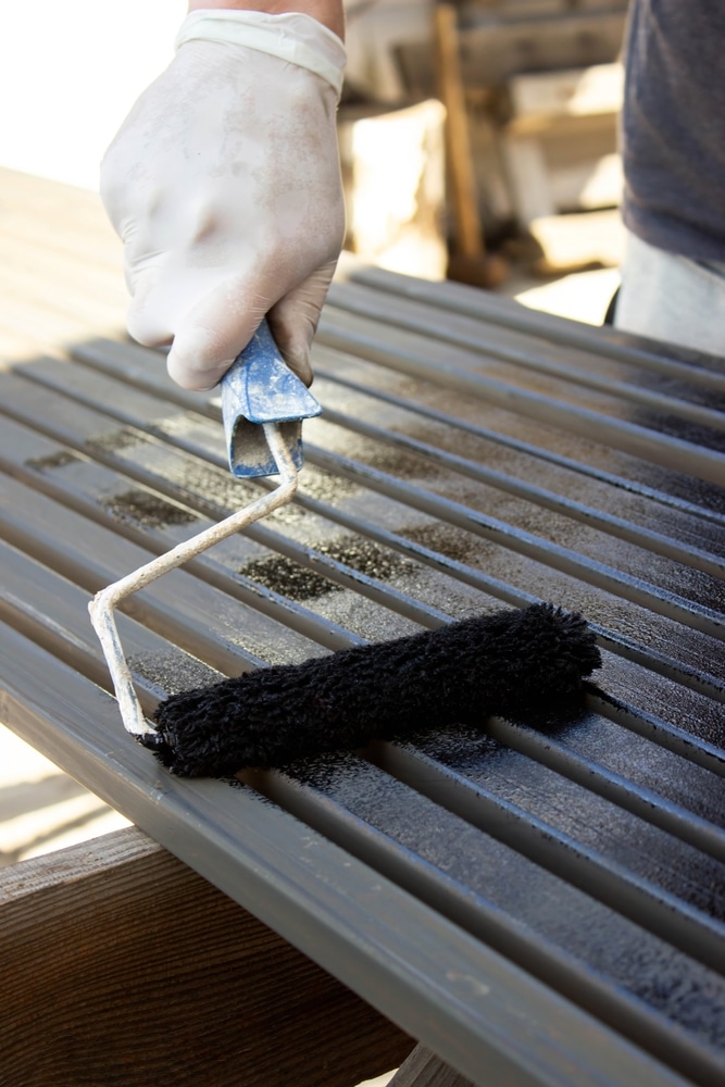 Rénovation extérieure : Peindre des lattes au mini rouleau Main gantée appliquant de la peinture noire sur des lattes métalliques grises à l'aide d'un mini rouleau. Travail de rénovation.