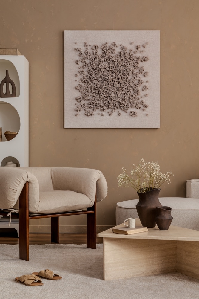 Salon design neutre : fauteuil beige et art mural texturé. Salon aux tons neutres : fauteuil beige en lin, table basse en travertin et art abstrait texturé sur mur taupe.
