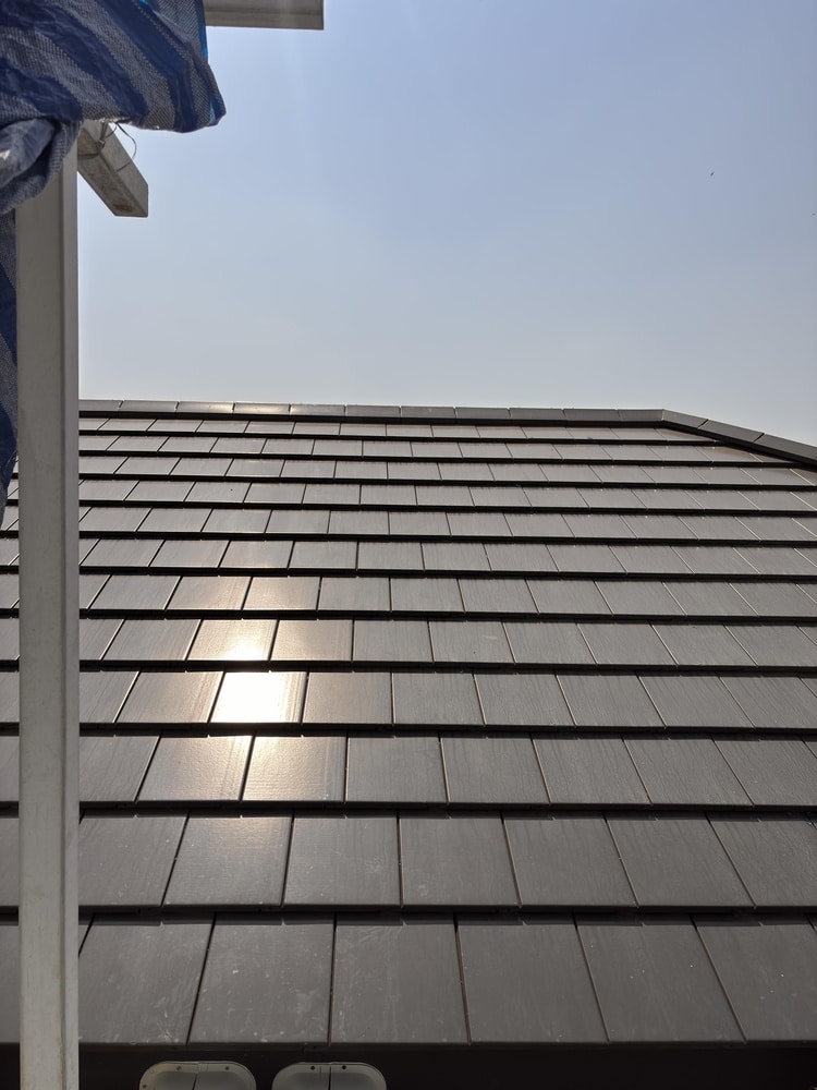 Installation de tuiles de toit sombres et modernes Toiture en tuiles modernes sombres et plates avec forte réflexion du soleil. Poteau de construction à gauche sous un ciel bleu.