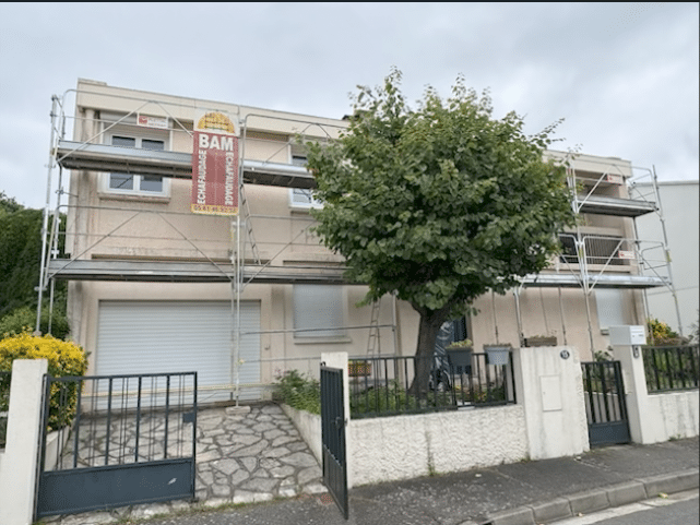 Échafaudage BAM pour rénovation de façade de maison Façade de maison en rénovation équipée d'un échafaudage BAM, avec un grand arbre feuillu et un garage.