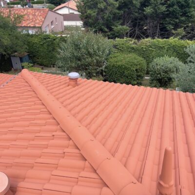 Toiture orange en tuiles terre cuite avec faîtage et épi décoratif.
